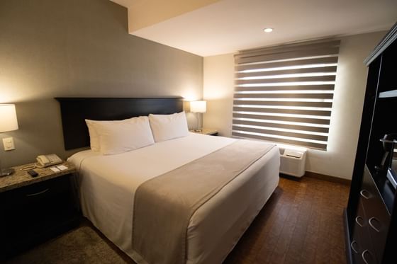 Cama frente a mueble de TV junto a ventana con persianas rayadas en la Habitación Ejecutiva de Araiza Hermosillo