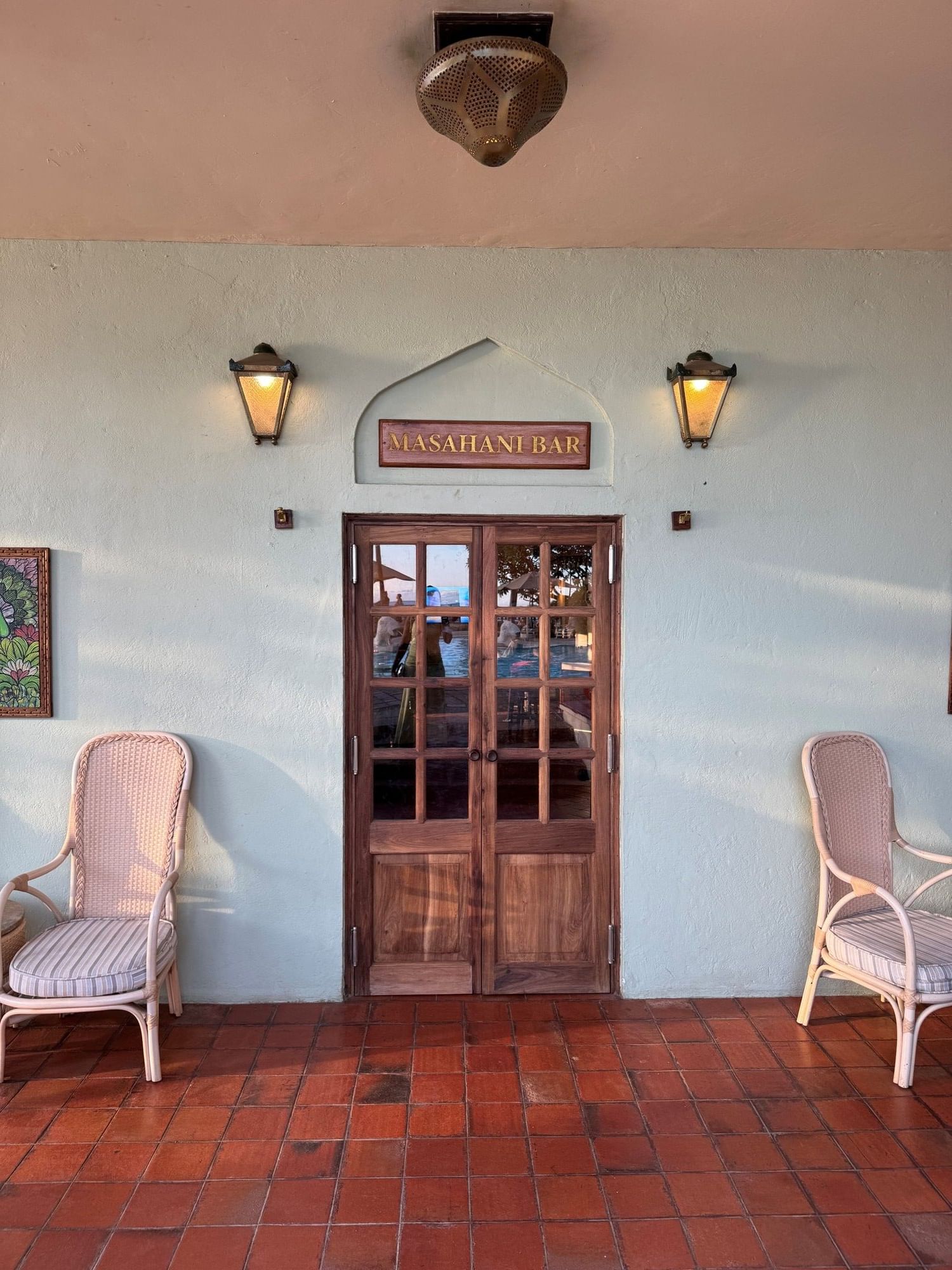 Entrance to Masahani Bar with wooden doors and rattan chairs at Zanzibar Serena Hotel.