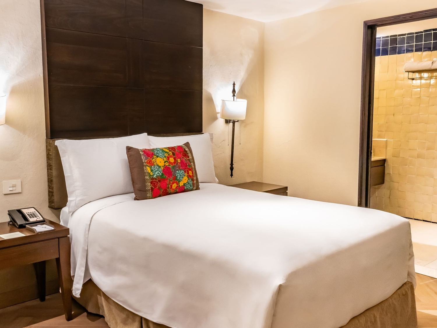 Double Novicia room with white bedding, dark wood headboard, and colorful accent pillow at Quinta Real Puebla.