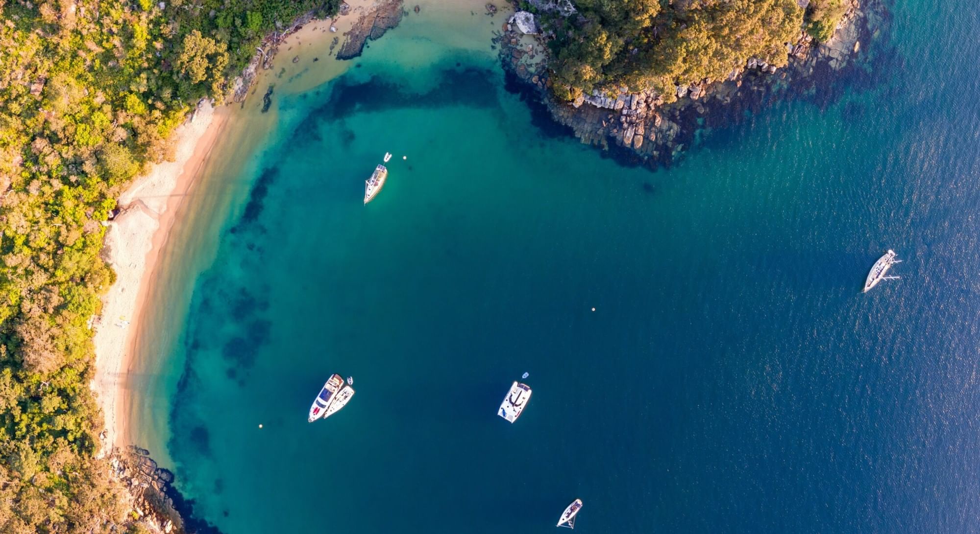 Store Beach at Elysium Hotels has a secluded sandy cove with turquoise water and boats surrounded by a dense forest