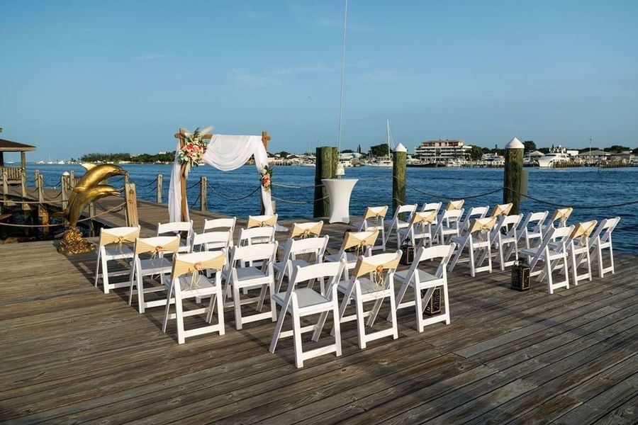 White chairs by a floral arch on a wooden pier surrounding blue harbor waters at Warwick Paradise Island Bahamas