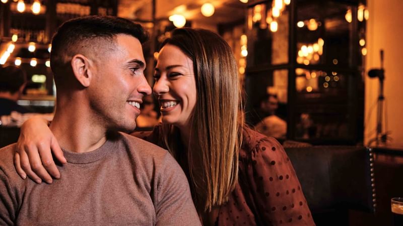 Couple sitting close in a dimly lit bar with a warm ambiance at Mercure Kooindah Waters