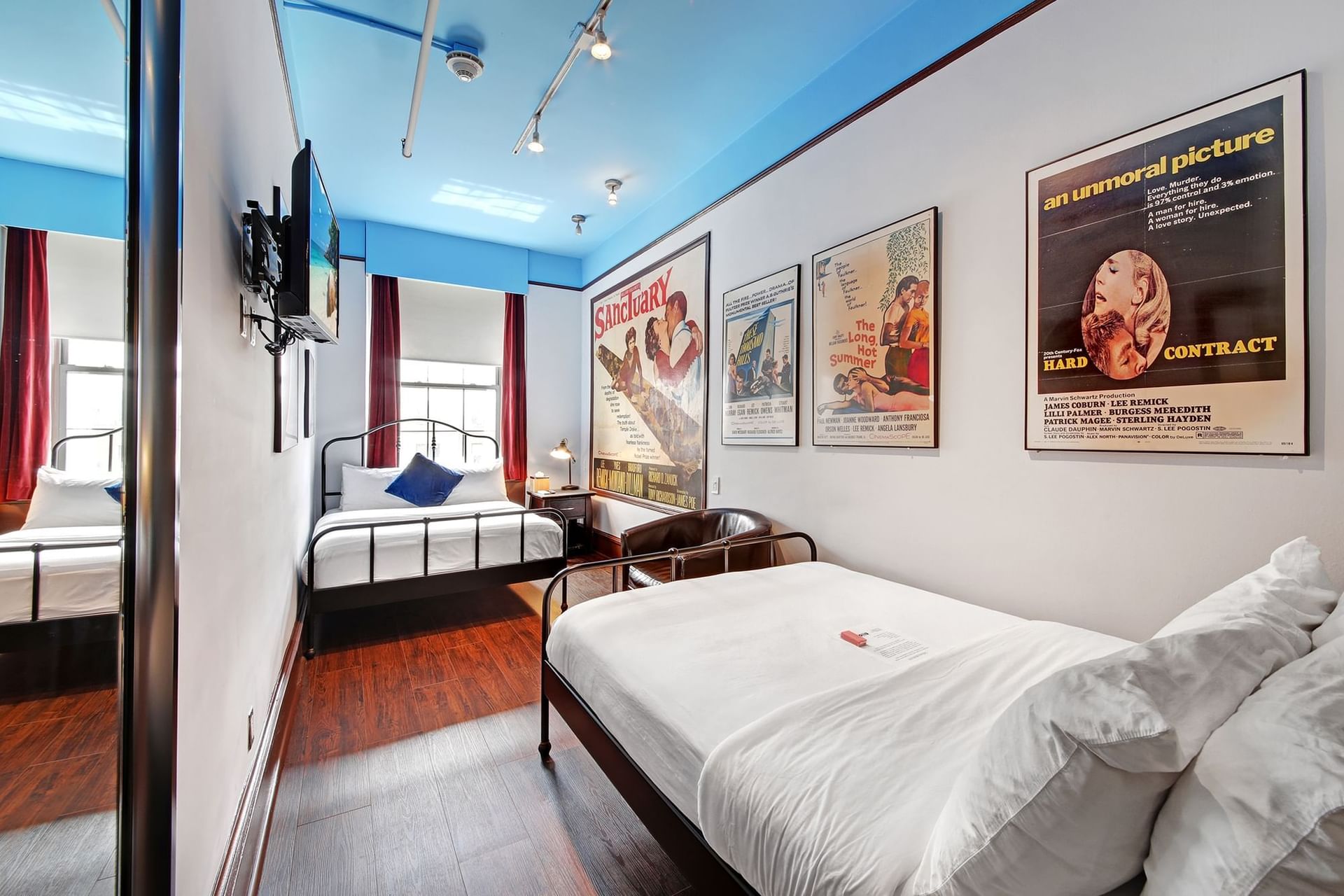 Quadruple Room at Chelsea Pines Inn with three beds, blue ceiling, hardwood floors, and vintage movie posters on the wall.