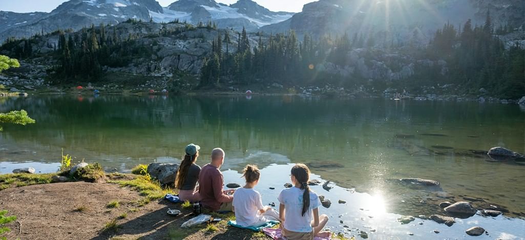 A family sits on towels by the river's edge in Canmore, enjoying the sun in spring.