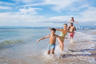 Family of four playing and running through shallow ocean waves on a sunny beach at Playa Los Arcos Puerto Vallarta