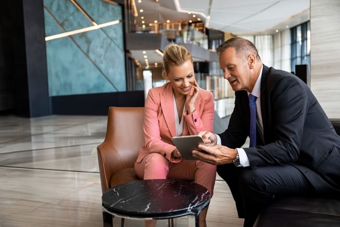 Two business professionals in suits reviewing documents using tablet together at modern office