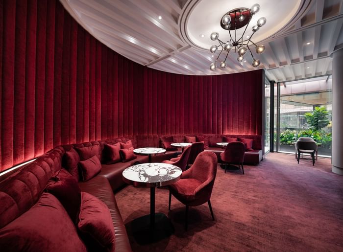 Red velvet sofas by marble tables under a globe chandelier in the stylish lounge at the Sofitel Sydney Wentworth