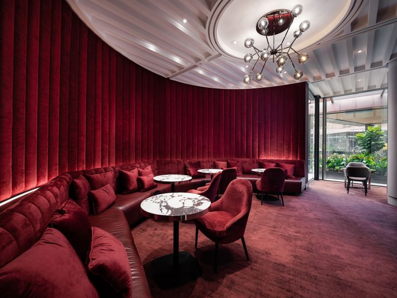 Modern lounge with red cushioned seating, round marble tables, and elegant chandelier, offering a cozy and stylish atmosphere
