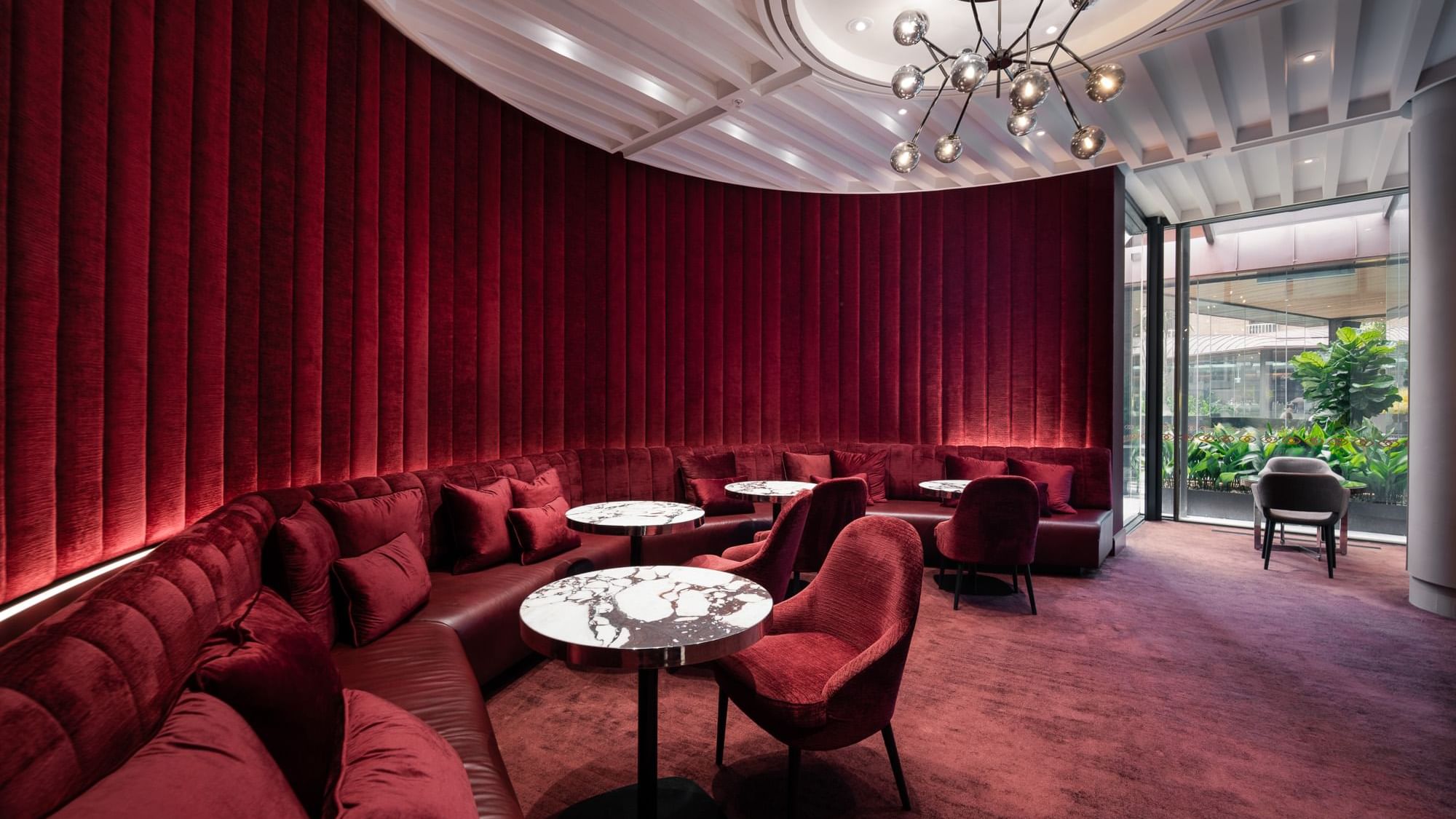 Modern lounge with red cushioned seating, round marble tables, and elegant chandelier, offering a cozy and stylish atmosphere