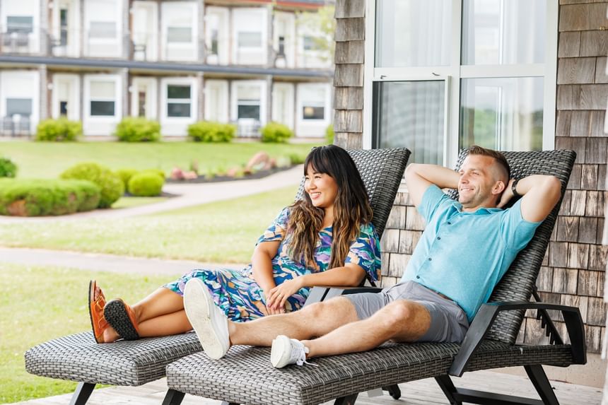 Happy couple relaxing on woven lounge chairs by a resort balcony wall area at Rodd Brudenell River Resort