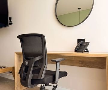 Black office chair facing wooden desk with phone below round mirror on white wall in a cozy room at Hotel B3 Sibelius