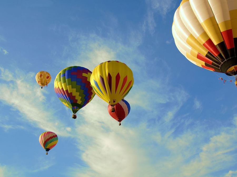 Colorful hot air balloons floating in a blue sky with light clouds near DAMAC Hotels & Resorts