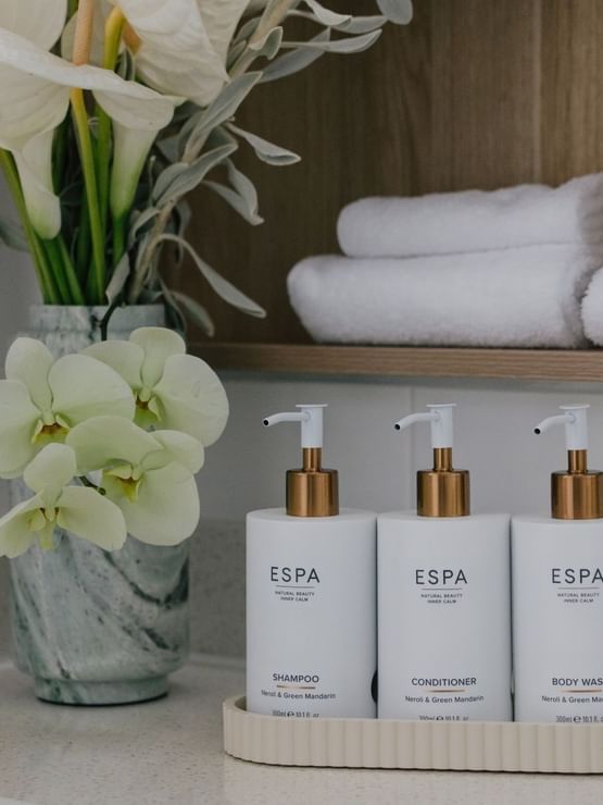 Amenity bottles placed by a vase of white orchids on a marble vanity under towels in Sunset Junior Suite at Elysium Manly