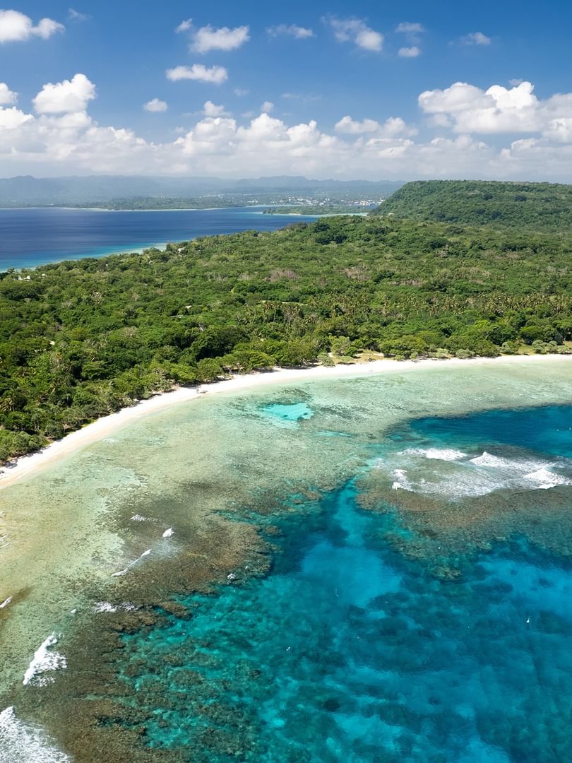 Aerial view of a Honeymoon Beach by turquoise coral reefs and lush green forests near Warwick Hotels & Resorts 