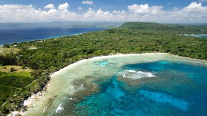 Aerial view of a Honeymoon Beach by turquoise coral reefs and lush green forests near Warwick Hotels & Resorts 