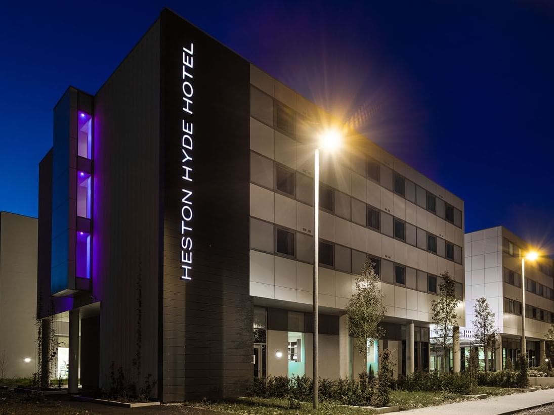 Heston Hyde Hotel exterior glowing at night with vibrant architectural lights and a peaceful setting