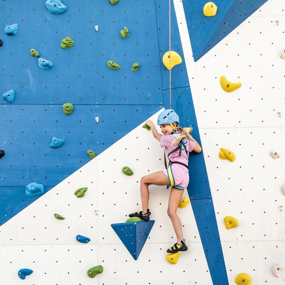 A young girl climbing a rock wall with blue and white background at Falkensteiner Family Resort Sicily