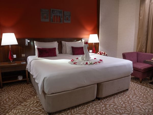 White bed with red pillows and swan towel decoration in Saja by Warwick Makkah hotel room.
