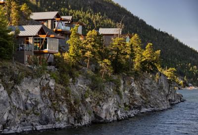 Modern houses with glass windows on a rocky hillside overlooking the water and mountain in the background.