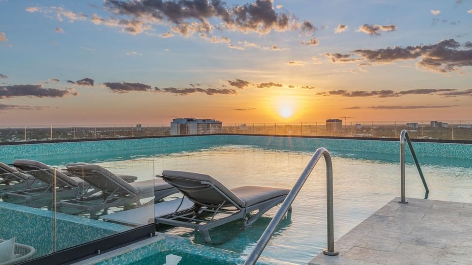Serene sunset view from the Camino Real Merida infinity pool featuring lounge chairs submerged in water