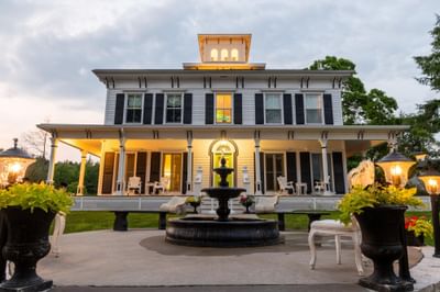 Exterior of The Roxbury with a fountain, porch, and elegant outdoor seating surrounded by lush greenery