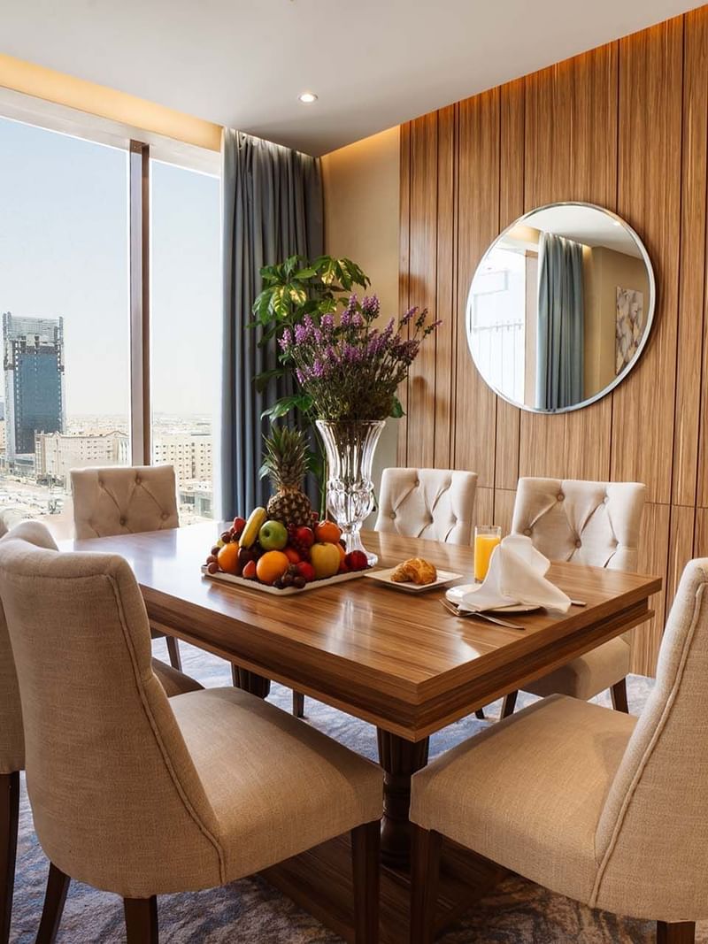 Royal Suite features Wooden dining table with chairs by a window under a round mirror at Cantonal Hotel by Warwick Riyadh
