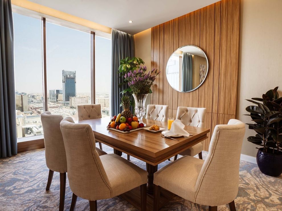Royal Suite features Wooden dining table with chairs by a window under a round mirror at Cantonal Hotel by Warwick Riyadh