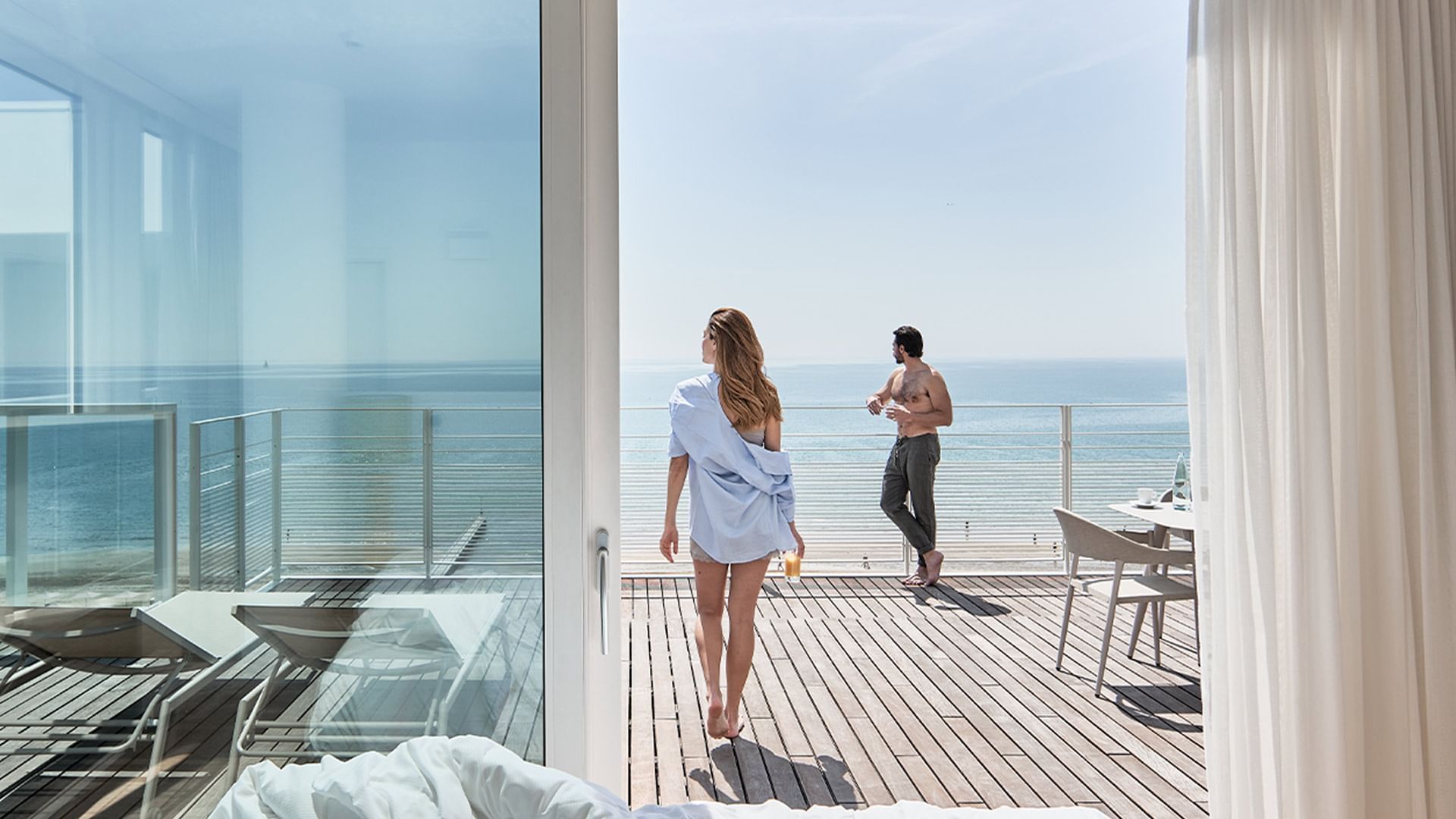Couple on a deck overlooking the ocean with outdoor furniture and a clear sky.