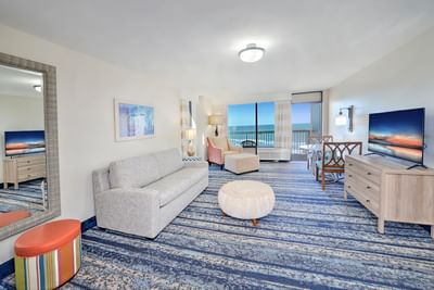 Ocean View Suite Kitchenette living room at the Daytona Bahama House with couch, chairs, TV, and balcony view of the ocean.