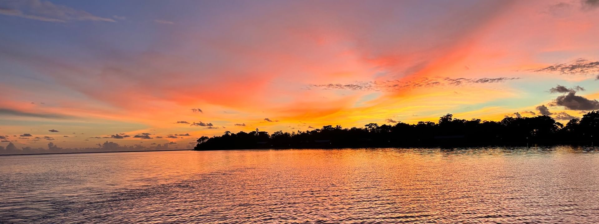 Vibrant sunset by a dark treeline, with orange light reflecting on rippling water near  Warwick Le Lagon - Vanuatu in Efate