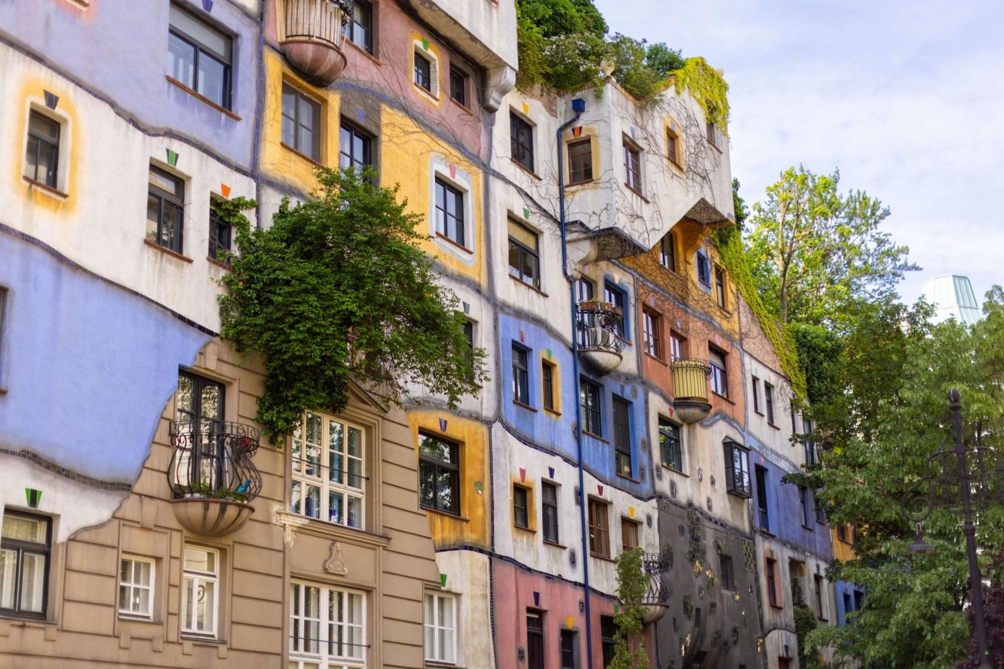 Buntes Hundertwasserhaus in Wien mit unregelmäßiger Fassade, begrünten Balkonen und verspielter Architektur.