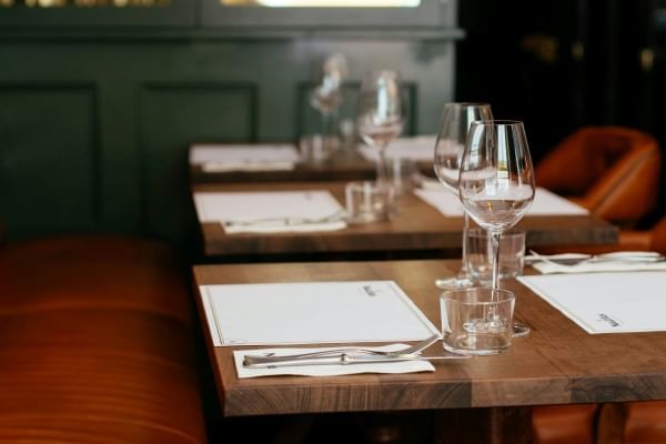 A short row of wooden tables set with menus, wine glasses, and silverware. 