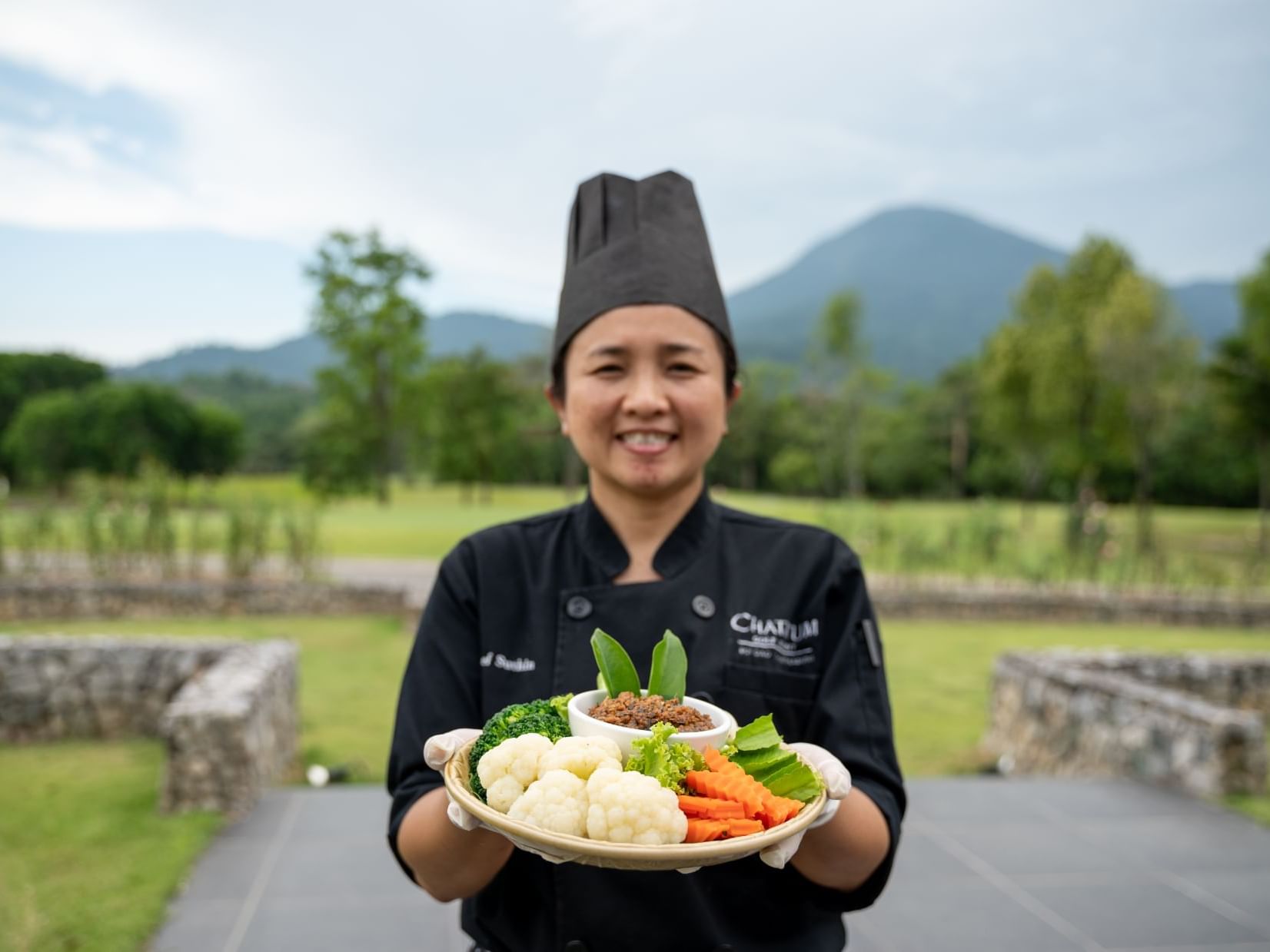 Chef holding a dish outdoors at Chatrium Hotels & Residences