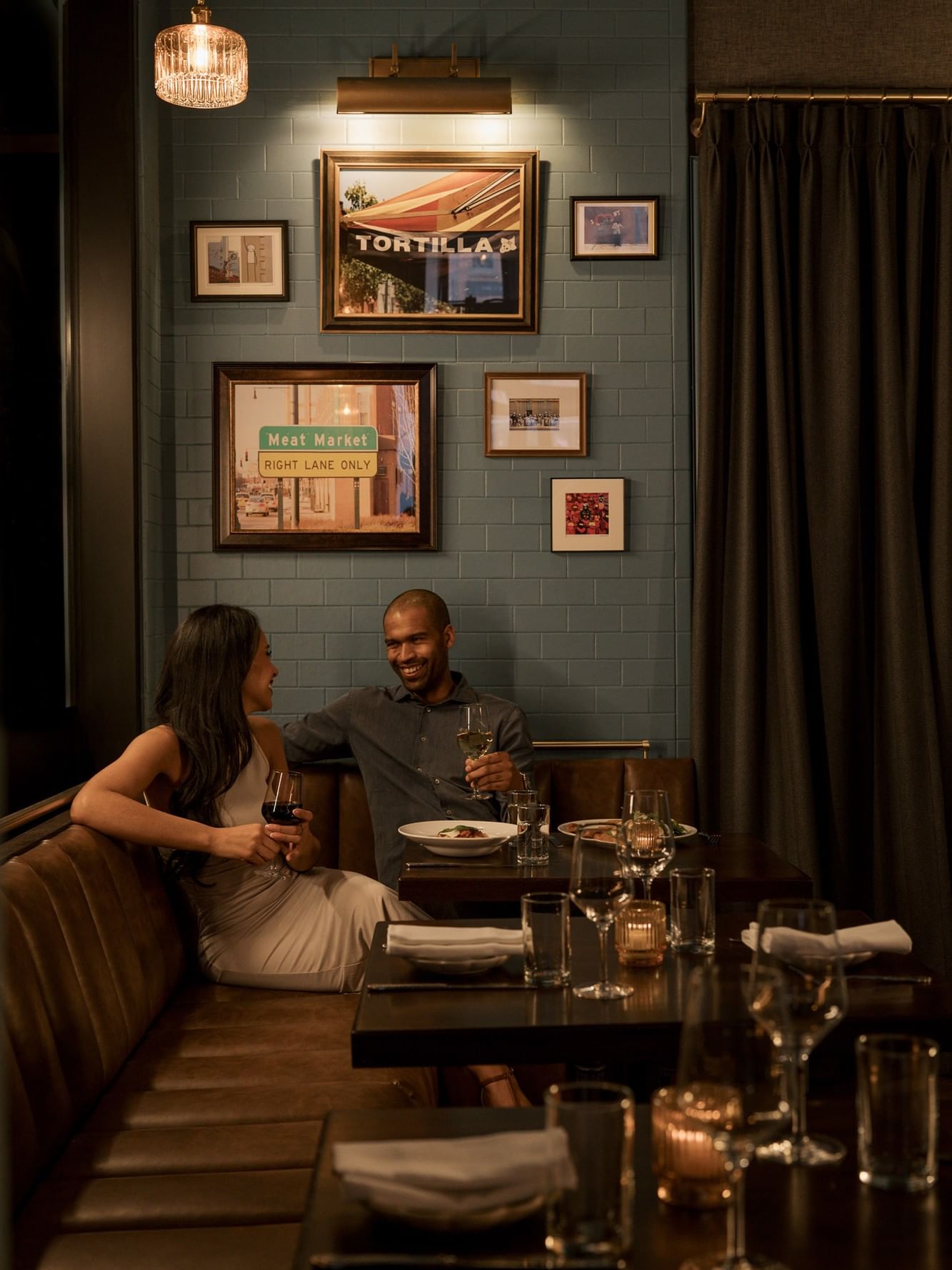 Couple enjoying dinner at Estelle's with vintage framed artwork on green tiled walls at Gansevoort Meatpacking NYC 