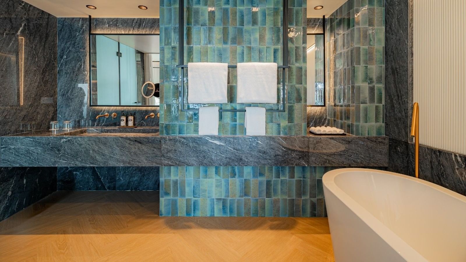 Banheiro elegante com azulejos azuis, pia de mármore, espelho grande e banheira branca.
