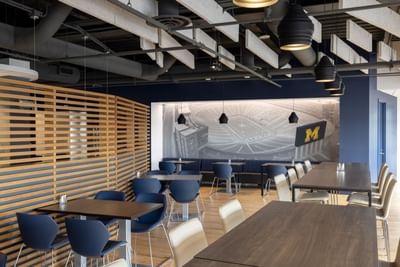 Modern restaurant with wooden tables and blue chairs, a mural of a stadium, and unique lighting at Aramark Ross