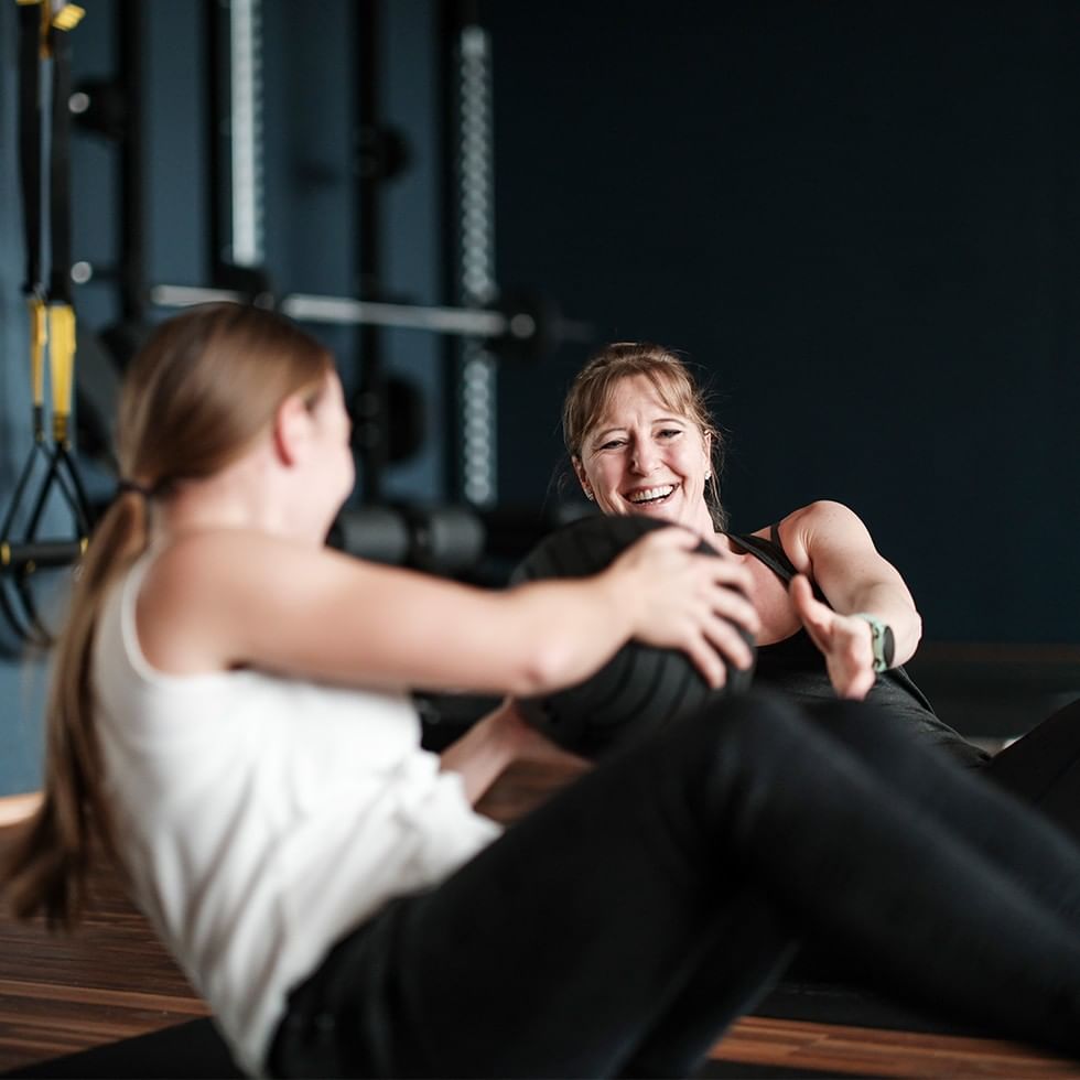 Two women using a medicine ball during Functional Power Weekends at the gym.