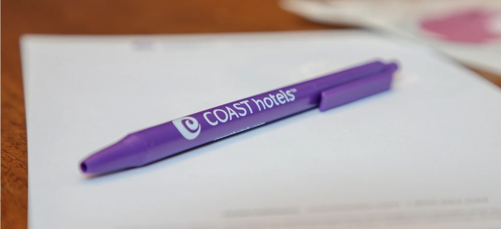 A close-up of a purple Coast Hotels branded pen resting on a sheet of paper, symbolizing professionalism, hospitality, and brand identity.