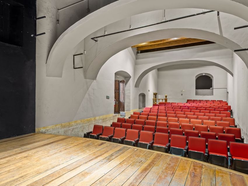 Small theater with red seating, white arched ceilings, and a wooden stage in Auditorio at Quinta Real Puebla