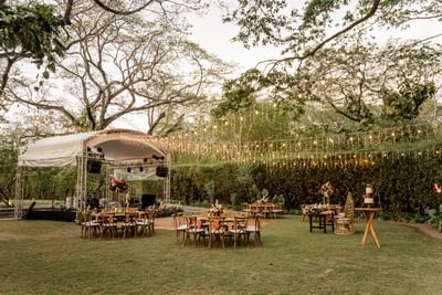 Outdoor event setting with tables, a stage and string lights among trees at El Mangroove Hotel
