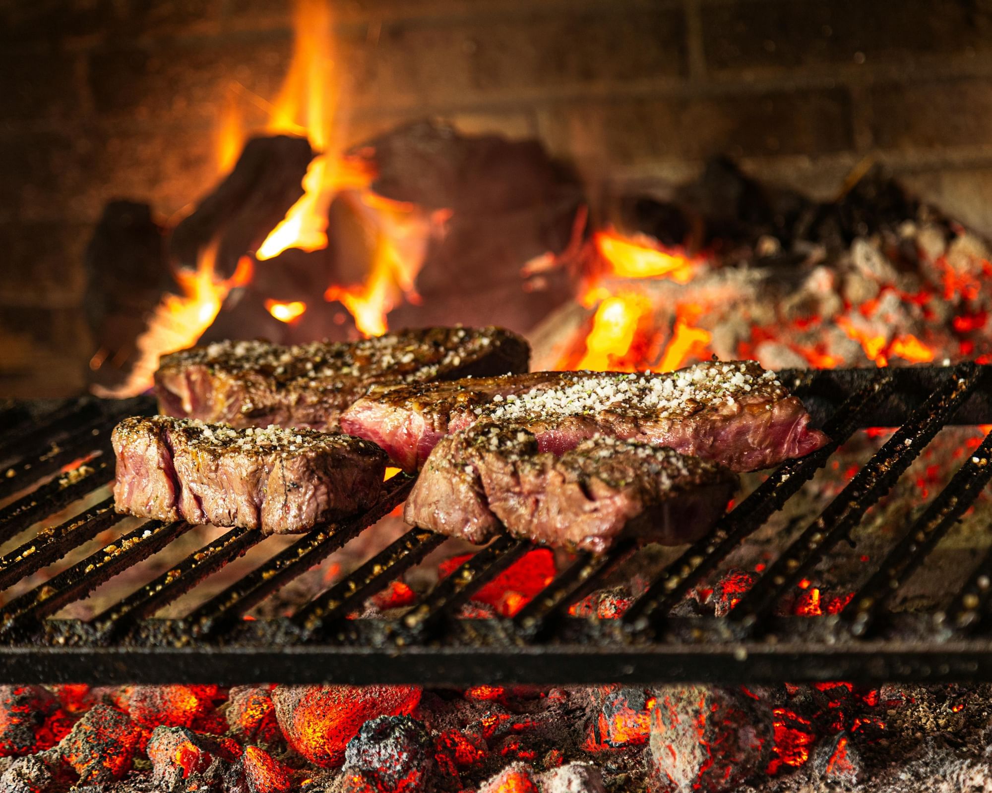 Steak grilling on a barbecue grill lightly covered in seasoning.