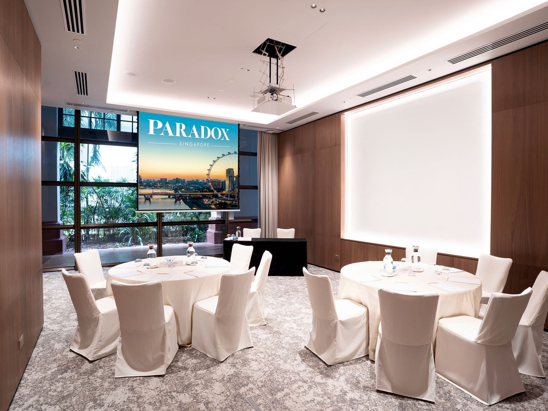Cluster setup in a meeting room at Paradox Singapore, featuring small groups of tables and chairs arranged for breakout discussions in a contemporary, professional setting.