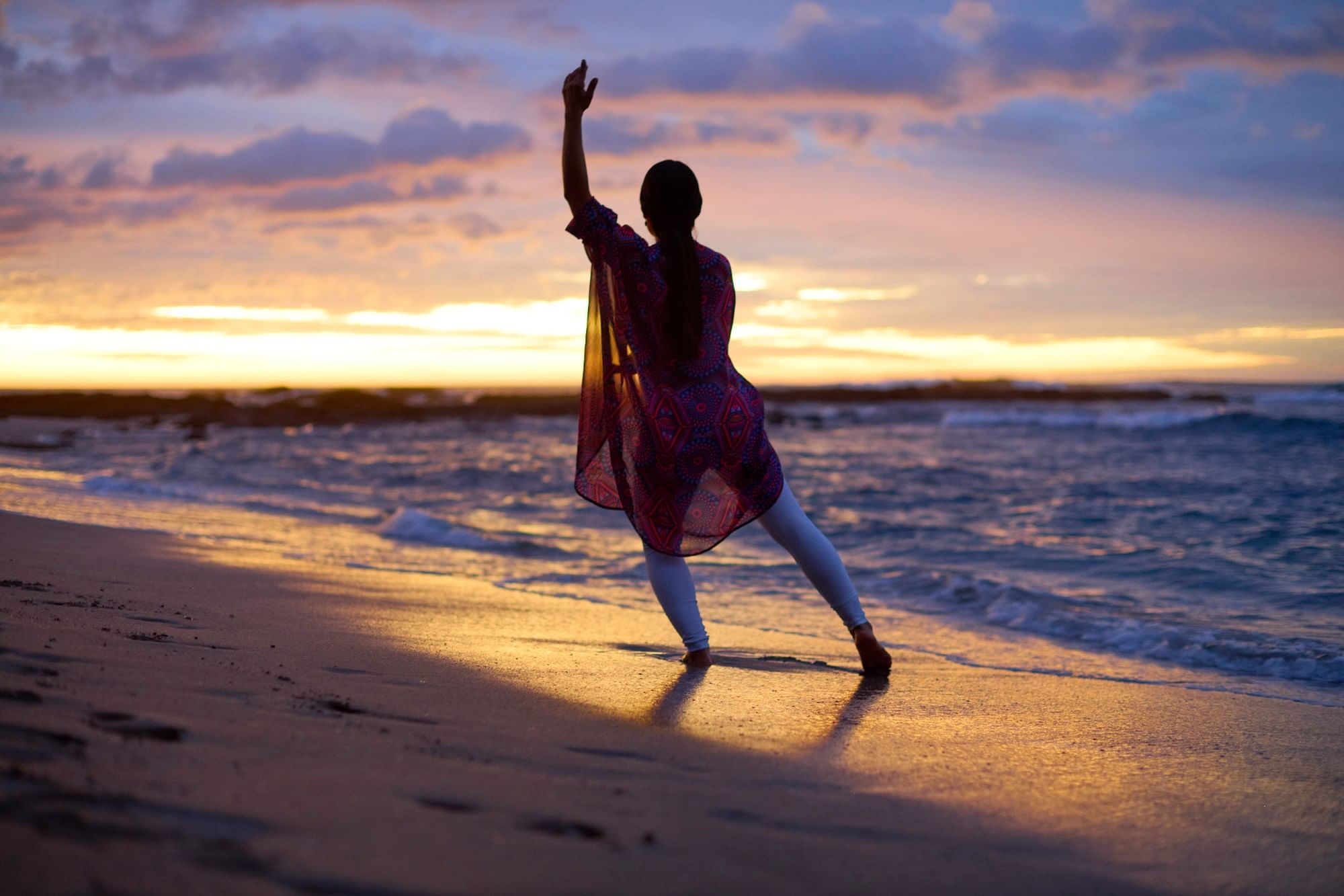 Woman dancing on the beach at sunset with purple clouds reflecting on the ocean near Cala Luna Boutique Hotel