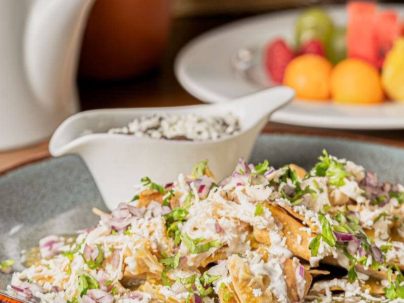 Close-up of chilaquiles topped with crumbled cheese and onions, served with creamy sauce at Fiesta Americana Travelty