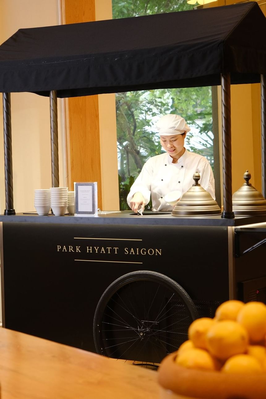 Chef standing behind a food cart with a black canopy featuring the Park Hyatt Saigon logo at Opera Restaurant