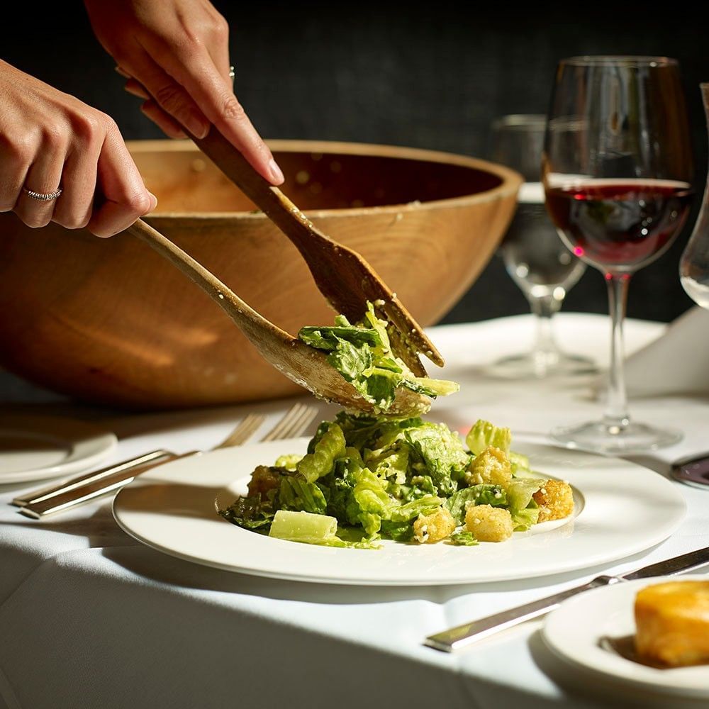 A Hy's Steakhouse staff member's hands preparing a Caesar salad from scratch 