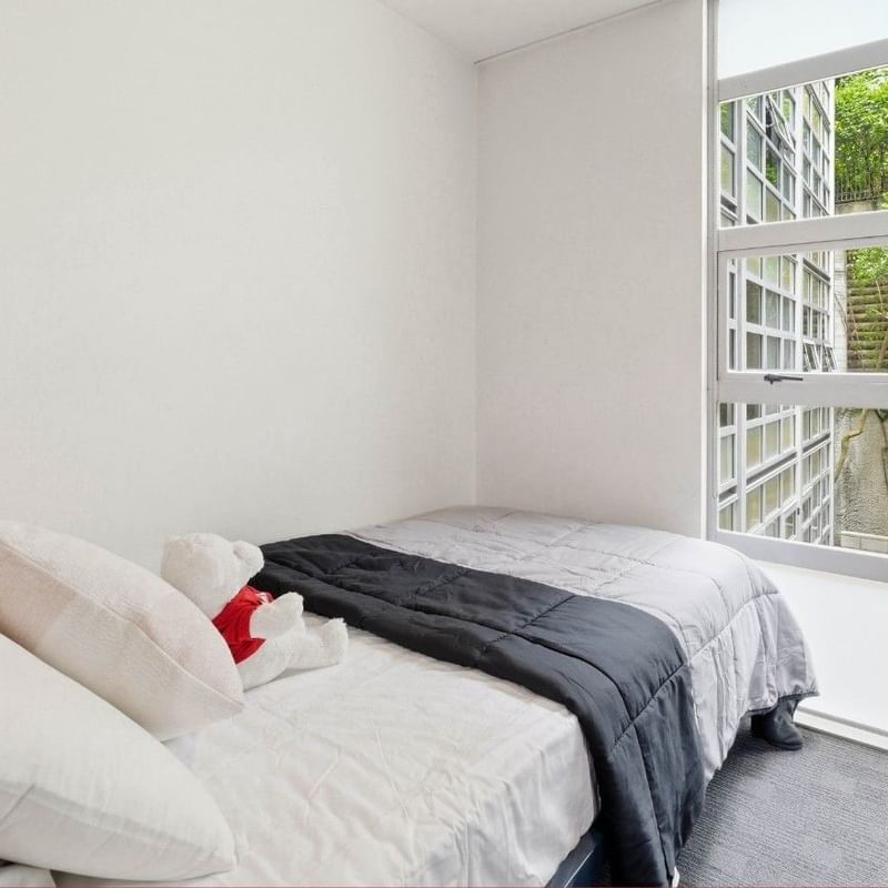 A cozy bedroom with a bed and a teddy bear near a large window at Student Living Auckland Beach.