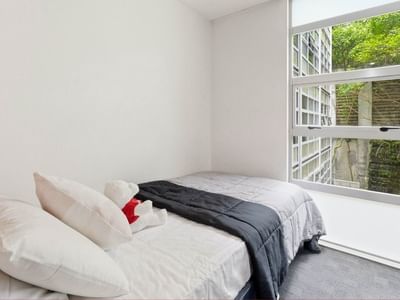 Cozy bedroom with white bedding and a plush teddy bear at Student Living Auckland Beach.