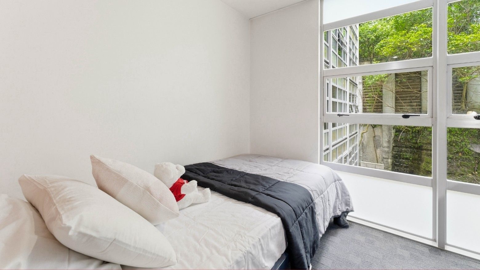 A cozy bedroom with a bed and a teddy bear near a large window at Student Living Auckland Beach.