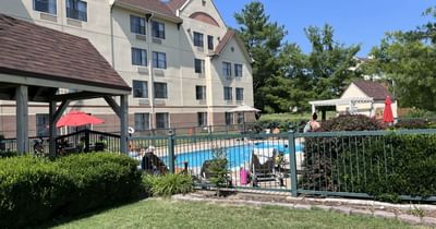 Fenced-in outdoor swimming pool at a hotel with lounge chairs and red umbrellas at Branson Hillside Hotel